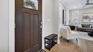 Ein modernes Wohnzimmer mit einer dunkelholzigen Tür, einem weißen Sessel, einem grauen Sofa und einem Deckenventilator.