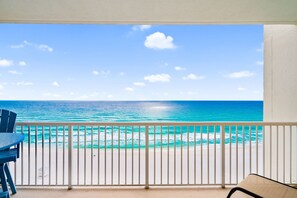 Un balcon avec vue sur l’océan, une balustrade blanche et une chaise bleue.