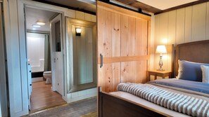 A bedroom with a wooden headboard, a bedside table with a lamp, and a bed with striped bedding. - Peaceful Family Friendly Private Lake Waterfront Home Close to Skiing and Hiking (Bennington)