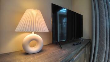 Una habitación moderna con una televisión de pantalla plana sobre un soporte de madera, una lámpara de mesa blanca con un diseño original y un control remoto en el soporte.