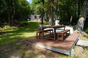A picnic table set up in a forested area with a house in the background. - Peaceful Family Friendly Private Lake Waterfront Home Close to Skiing and Hiking (Bennington)
