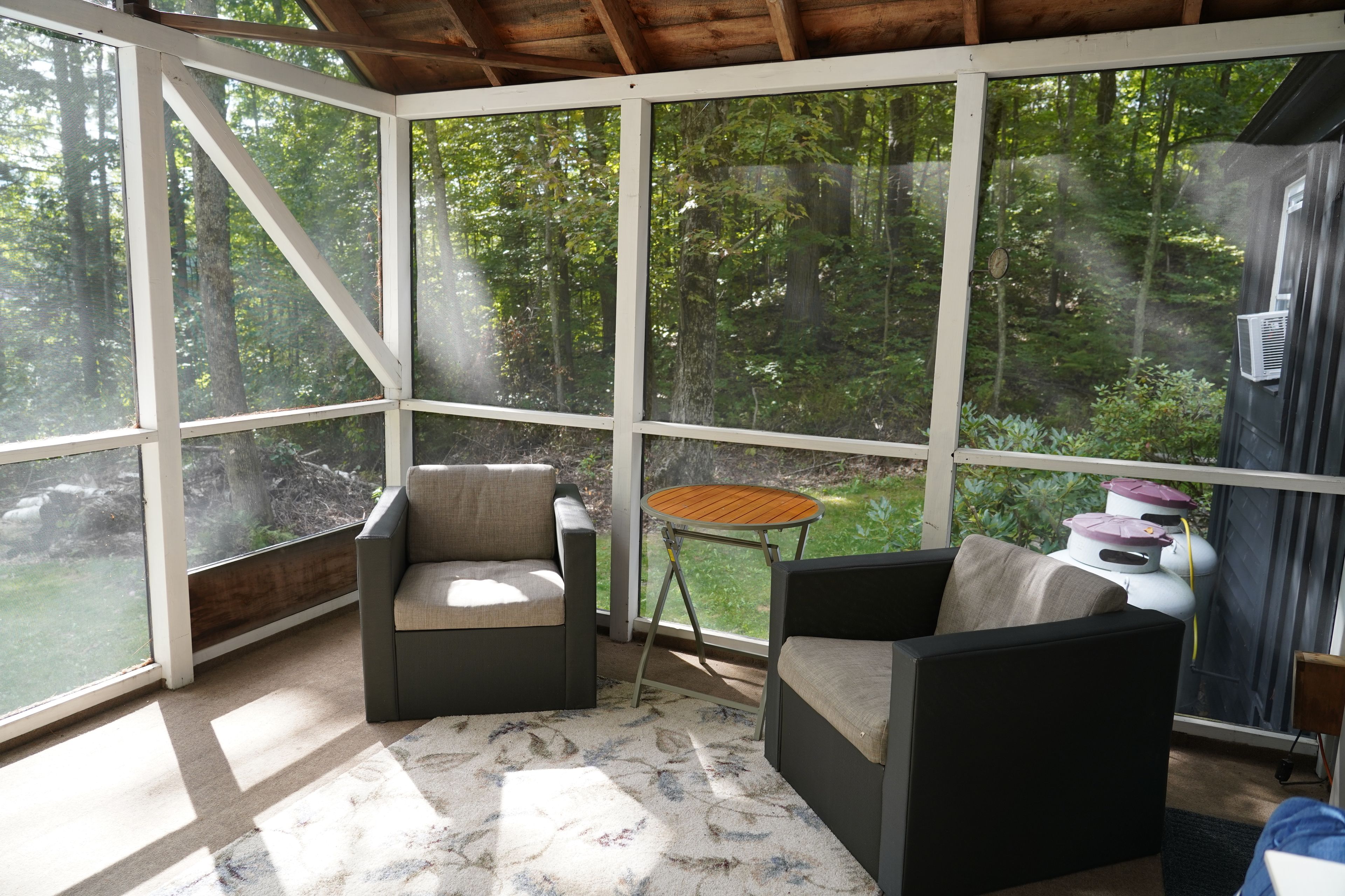 Une véranda donnant sur une forêt, deux fauteuils, une petite table et un radiateur.