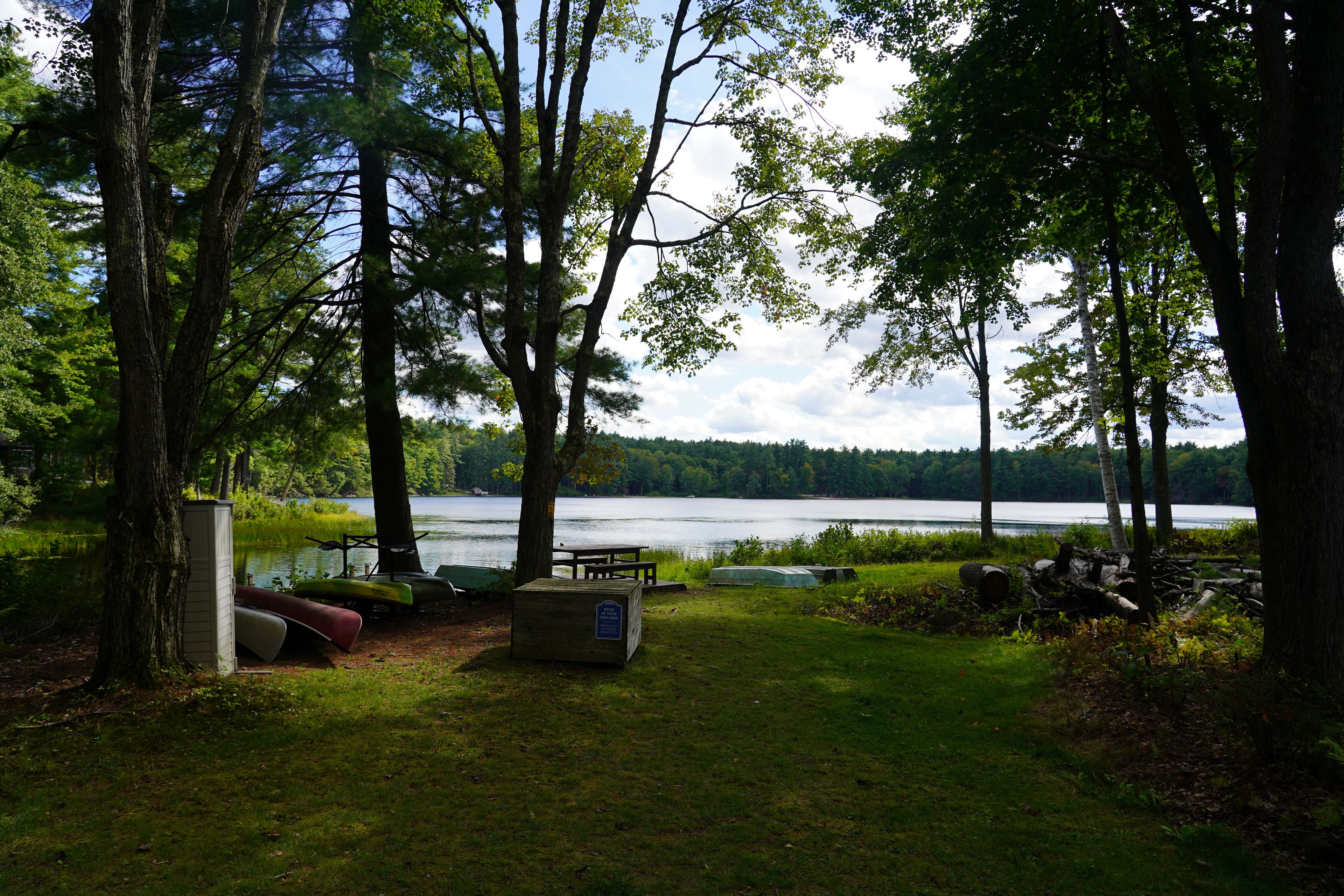 A lakeside campsite with a picnic table, canoe storage, and a small shed.