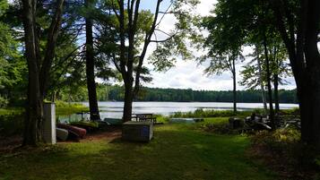 A lakeside campsite with a picnic table, canoe storage, and a small shed.