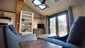 A cozy living room with a fireplace, a TV, and a large window offering a view of the outdoors. - Peaceful Family Friendly Private Lake Waterfront Home Close to Beach and Hiking (Bennington)