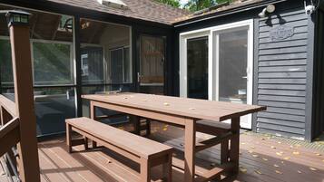 Une terrasse en bois avec une table de pique-nique et un banc, un patio couvert et un bâtiment sur lequel est affiché un panneau indiquant « MAISON AU BORD DU LAC ».