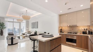 A modern kitchen with a central island, wooden cabinets, and stainless steel appliances. There is a dining area with a sofa and a coffee table. - Stayshort - Lovely 3 Bed in Downtown Sleeps 5 With Balcony (Dubai)