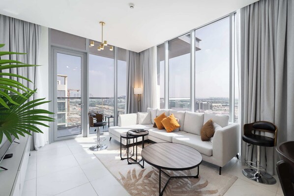 A modern living room with a white sofa, a round coffee table, and a view of a cityscape through large windows. - Stayshort - 1 Bed Unit in Meydan Sleeps 2 With Balcony (Dubai)