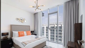 A modern bedroom with a large bed, a nightstand, a desk, a chandelier, and a view of the city through large windows. - Stayshort - 1 Bed Unit in Meydan Sleeps 2 With Balcony (Dubai)