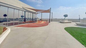 A rooftop terrace with a glass enclosure, outdoor seating, and a landscaped area with a tree. - Stayshort - 1 Bed Unit in Meydan Sleeps 2 With Balcony (Dubai)