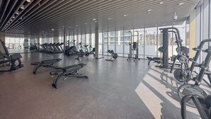 A spacious gym with various exercise equipment, large windows, and a modern ceiling design. - Stayshort - 1 Bed Unit in Meydan Sleeps 2 With Balcony (Dubai)