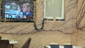 Un intérieur moderne avec un mur en marbre, un téléviseur à écran plat diffusant une émission, une petite fenêtre et un comptoir d’accueil.