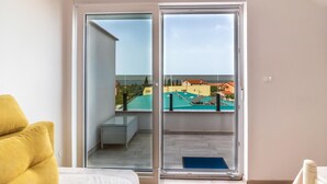 A room with a sliding glass door leading to a balcony with a view of buildings and a pool. - Stunning apartment in Peroj with house a panoramic view (Peroj)