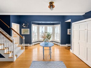 Une pièce avec un escalier en bois, une table ronde ornée d’un vase, et une vue dégagée grâce à de grandes fenêtres.