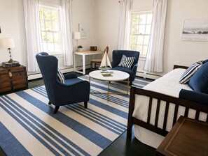 A room with a bed, two armchairs, a small table, a lamp, a radio, a plant, and a view of the outdoors through a window. - Charming Coastal Suite (Freeport)