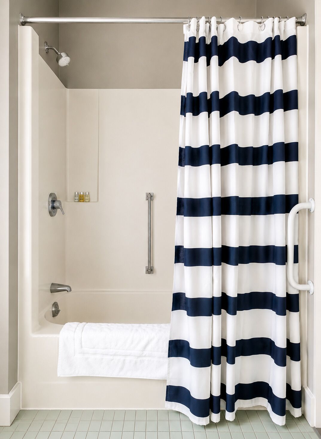 A shower with a striped curtain, a handheld showerhead, and a towel rack.