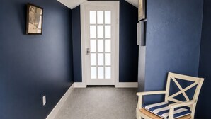 Ein Zimmer mit dunkelblauen Wänden, einer weißen Tür, einem gerahmten Bild, einem Holzstuhl und einem kleinen Tisch.