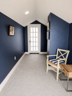 A room with dark blue walls, a white door, a framed picture, a wooden chair, and a small table. - Charming Coastal Suite (Freeport)