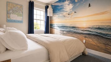 A bedroom with a large mural of a sunset over the ocean, a bed with white bedding, a map on the wall, and a window with curtains.