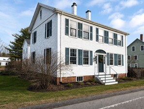 A two-story white house with a brick foundation, green shutters, and a front porch. - Charming Coastal Suite (Freeport)