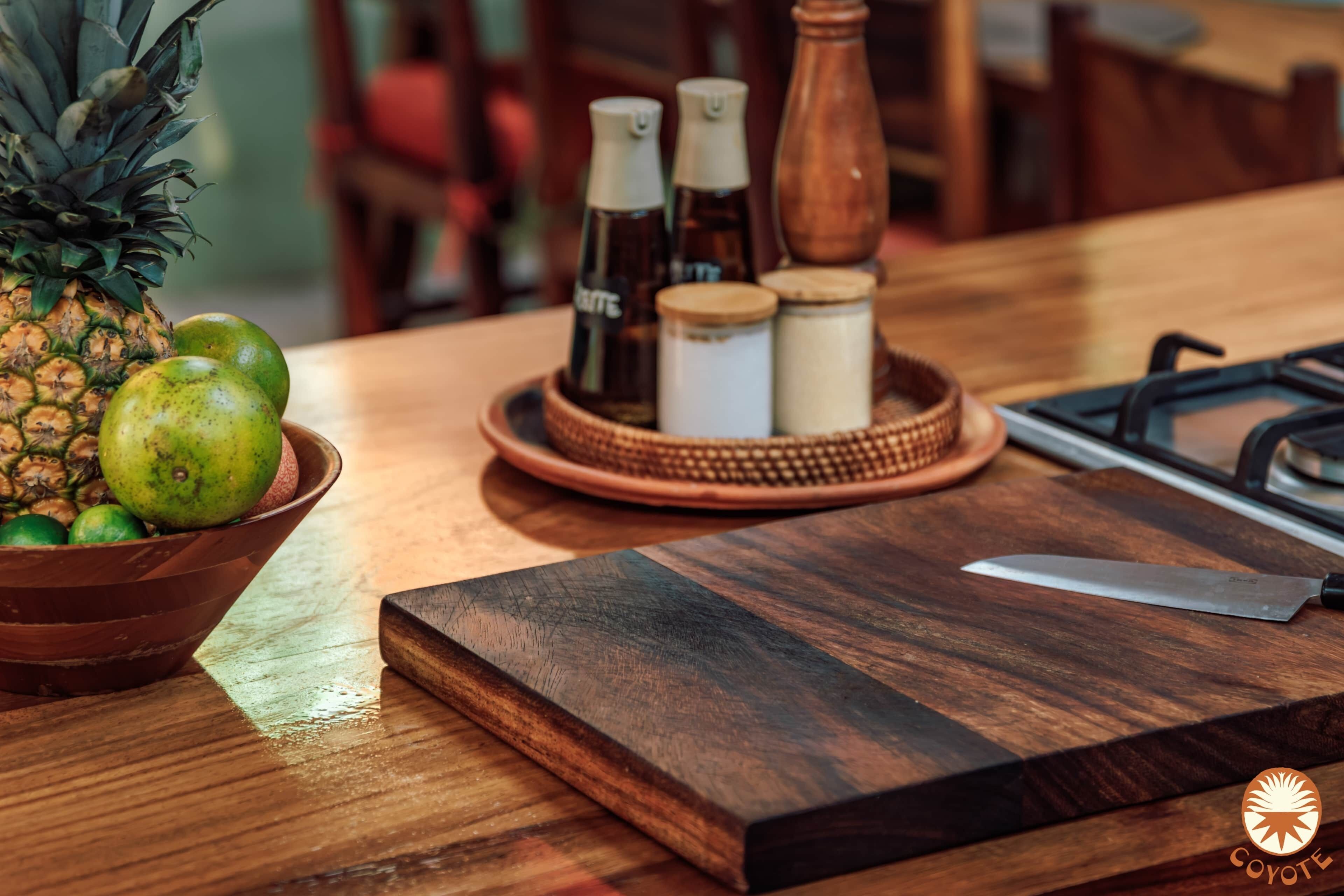Une planche à découper en bois, un couteau, un saladier rempli de fruits et des condiments sur une table.