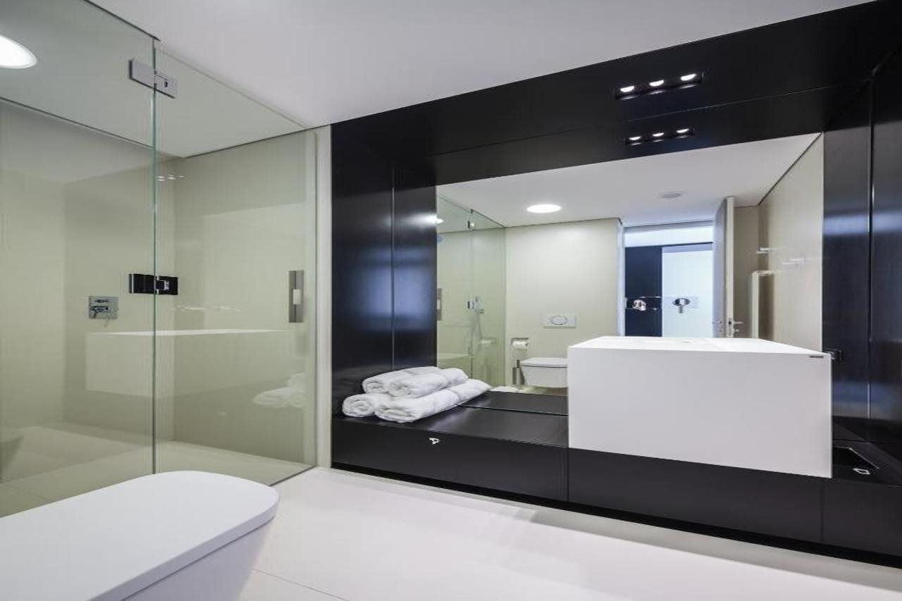 A modern bathroom with a glass shower enclosure, a white toilet, and a large mirror reflecting a bathroom vanity with a sink and towel rack.