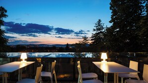 An outdoor dining area with tables and chairs, a lamp, and a view of the city skyline at dusk. - Hotel Privo (Târgu Mureș)