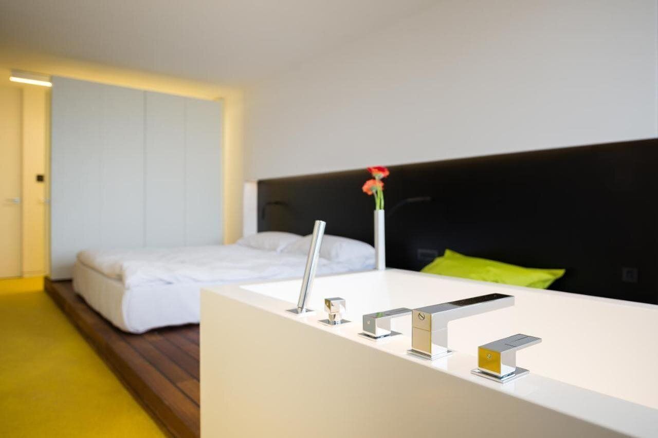 A modern hotel room with a white bed, a black headboard, and a white bedside table with a vase of flowers.