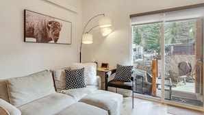 Ein modernes Wohnzimmer mit einer Couch, zwei Sesseln, einem Tisch und einem Laptop. Ein großes Fenster bietet einen Ausblick ins Freie.