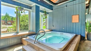 Ein Wellnessraum mit Whirlpool, Holzbänken und großen Fenstern mit Blick ins Freie.
