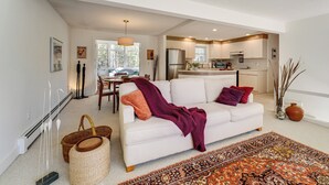 Ein geräumiger Wohnbereich mit einem weißen Sofa, einem gemusterten Teppich und einer Küche im Hintergrund.