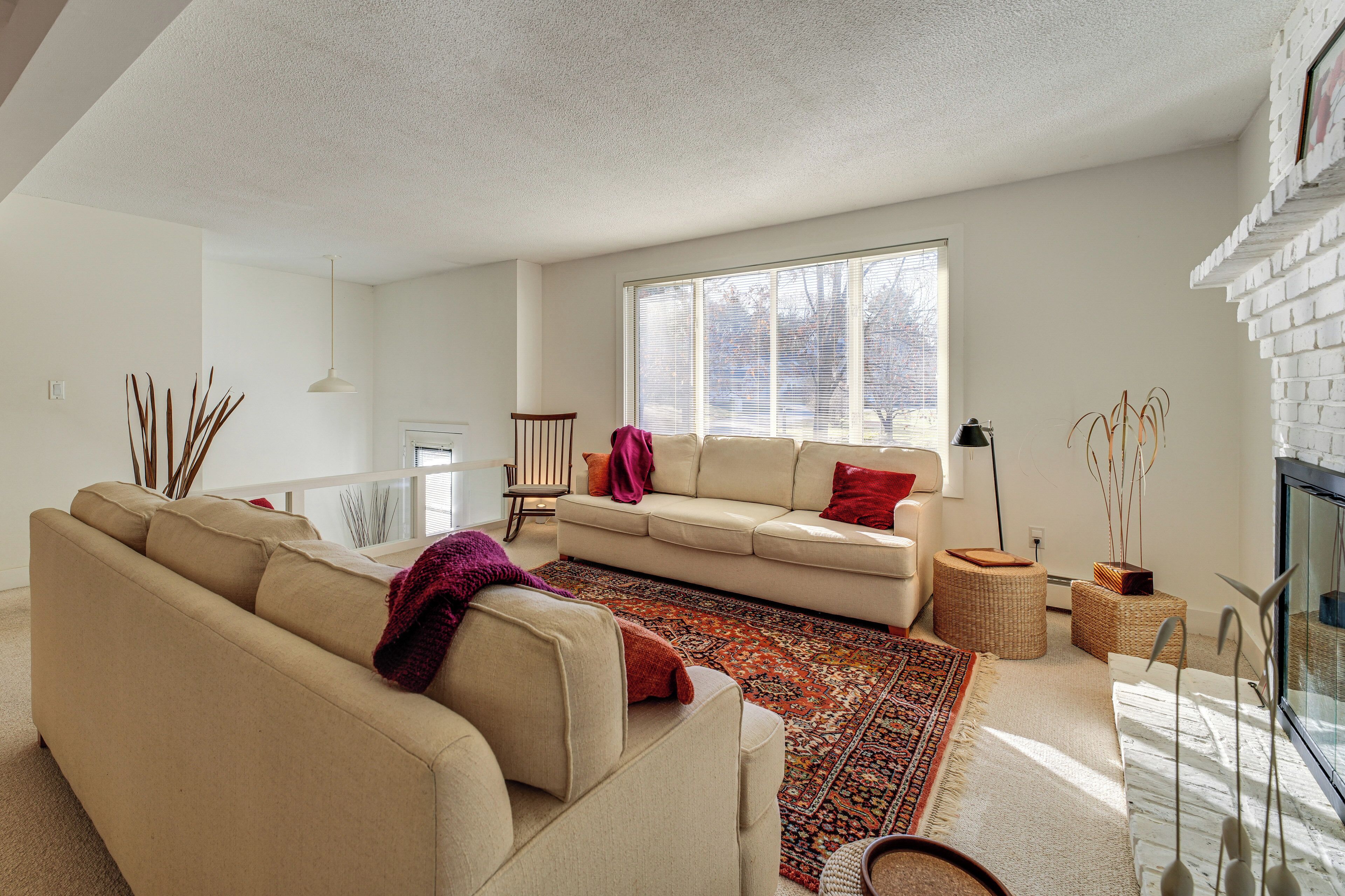 A modern living room with a beige sofa, a patterned rug, and a large window providing natural light.
