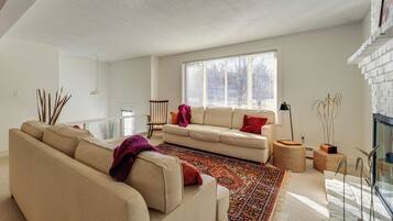 A modern living room with a beige sofa, a patterned rug, and a large window providing natural light.