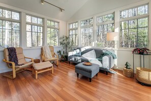 Ein geräumiges Wohnzimmer mit großen Fenstern, einem Sofa, einem Sessel und einem kleinen Tisch.