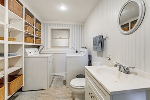 Casa de banho compacta e bem organizada, com máquina de lavar e secar integradas, um espelho grande e estantes para arrumação.