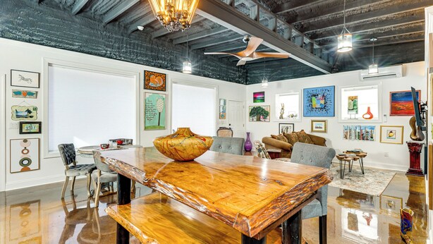 Une pièce spacieuse avec une table à manger en bois, des chaises, un ventilateur de plafond et des œuvres d’art accrochées aux murs.