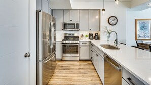 Una cocina moderna con electrodomésticos de acero inoxidable, armarios blancos y piso de madera.