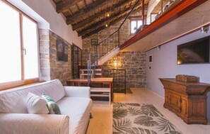 Ein gemütliches Wohnzimmer mit Steinwand, Holztreppe, weißem Sofa und Holzschrank.
