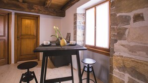 Ein gemütlicher Raum mit Holztür, Steinwand und Fenster. Es steht ein Tisch mit einer Blumenvase und einer Tasse darauf.
