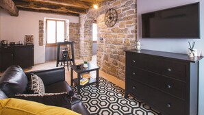 Ein gemütliches Wohnzimmer mit Steinwand, einer schwarzen Ledersofa, Holzboden und einem Flachbildfernseher.