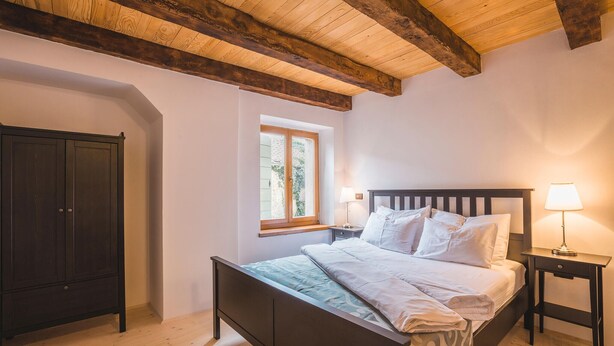 Un dormitorio con cama, mesita de noche, lámpara, armario y ventana.