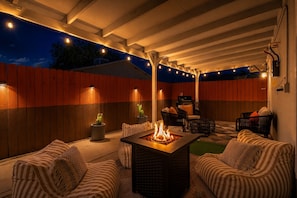En udendørs terrasse med bålsted, siddepladser og lyskæder.