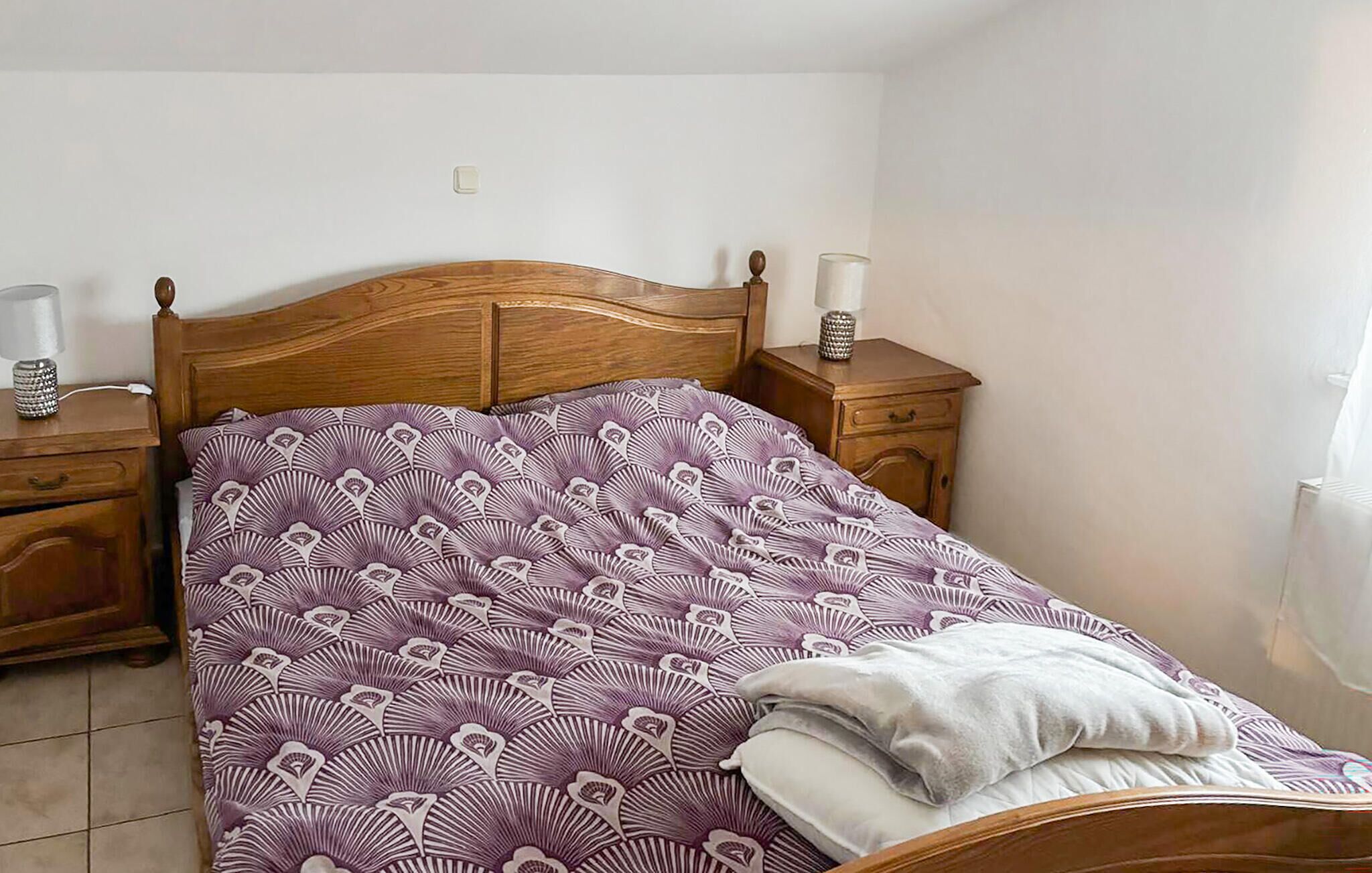 Una camera da letto con una struttura letto in legno, una coperta a motivi, due comodini con lampade e un tavolino da notte con lampada.