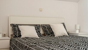 Quarto com uma cama coberta por um edredom com padrão de folhas em preto e branco, uma cabeceira branca e duas almofadas brancas.