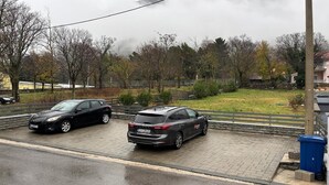 Uma área de estacionamento com dois carros estacionados em superfície pavimentada, cercada por árvores e um gramado.