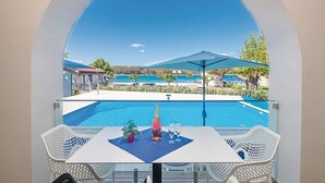 A balcony with a pool, white chairs, a table, and a bottle of champagne. - Lovely apartment in Punat with swimming pool (Punat)