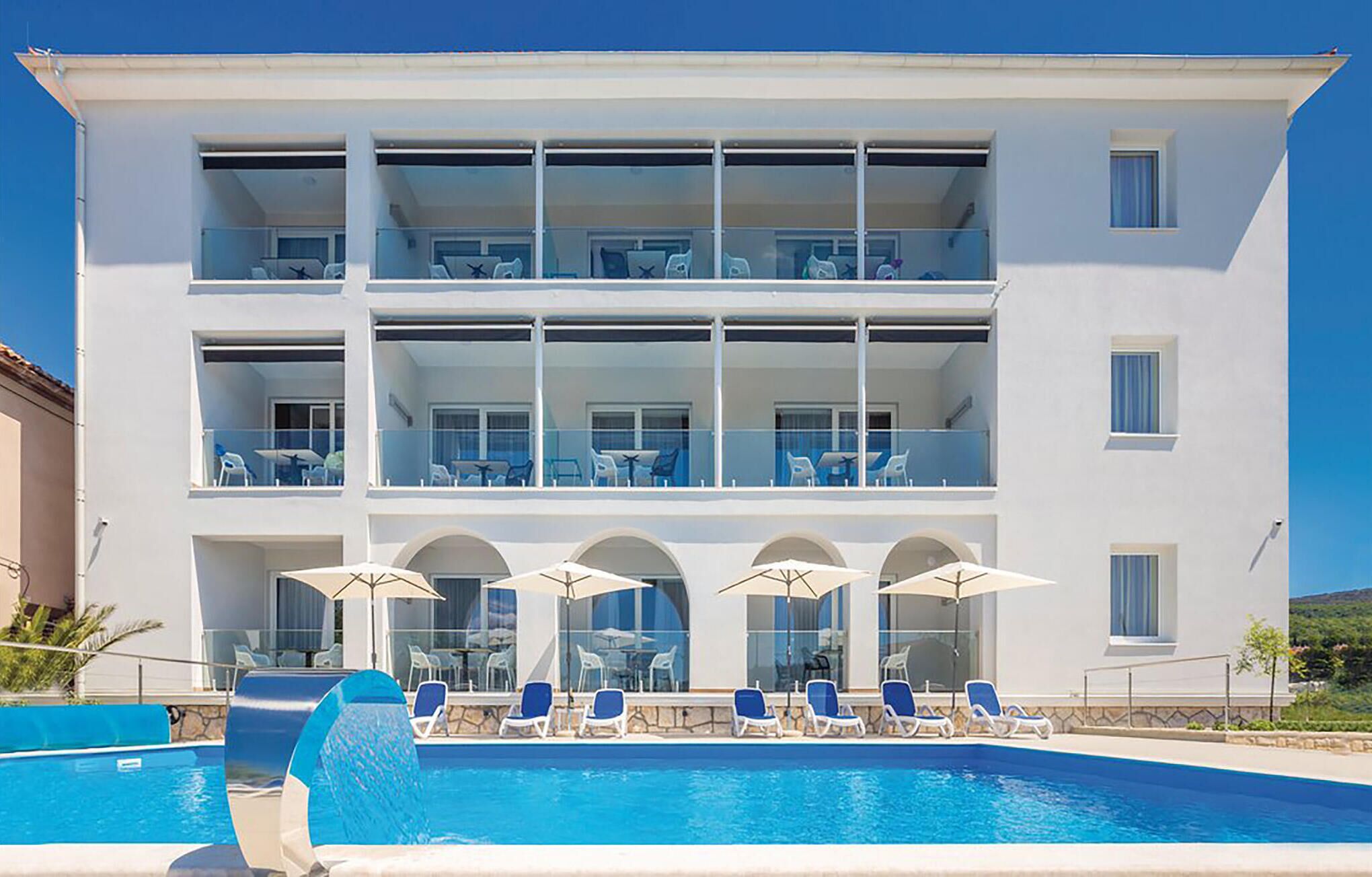 Un hôtel de deux étages doté d’une piscine, d’un espace extérieur aménagé et surplombant un ciel d’un bleu limpide.