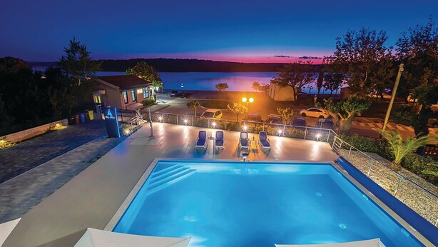 Ein Swimmingpool mit Liegestühlen und Blick auf ein Gewässer im Abenddämmerung.