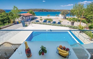 A poolside view with a clear view of the sea, a table with a bottle, a plant, and a fruit basket. - Cozy apartment in Punat with swimming pool (Punat)