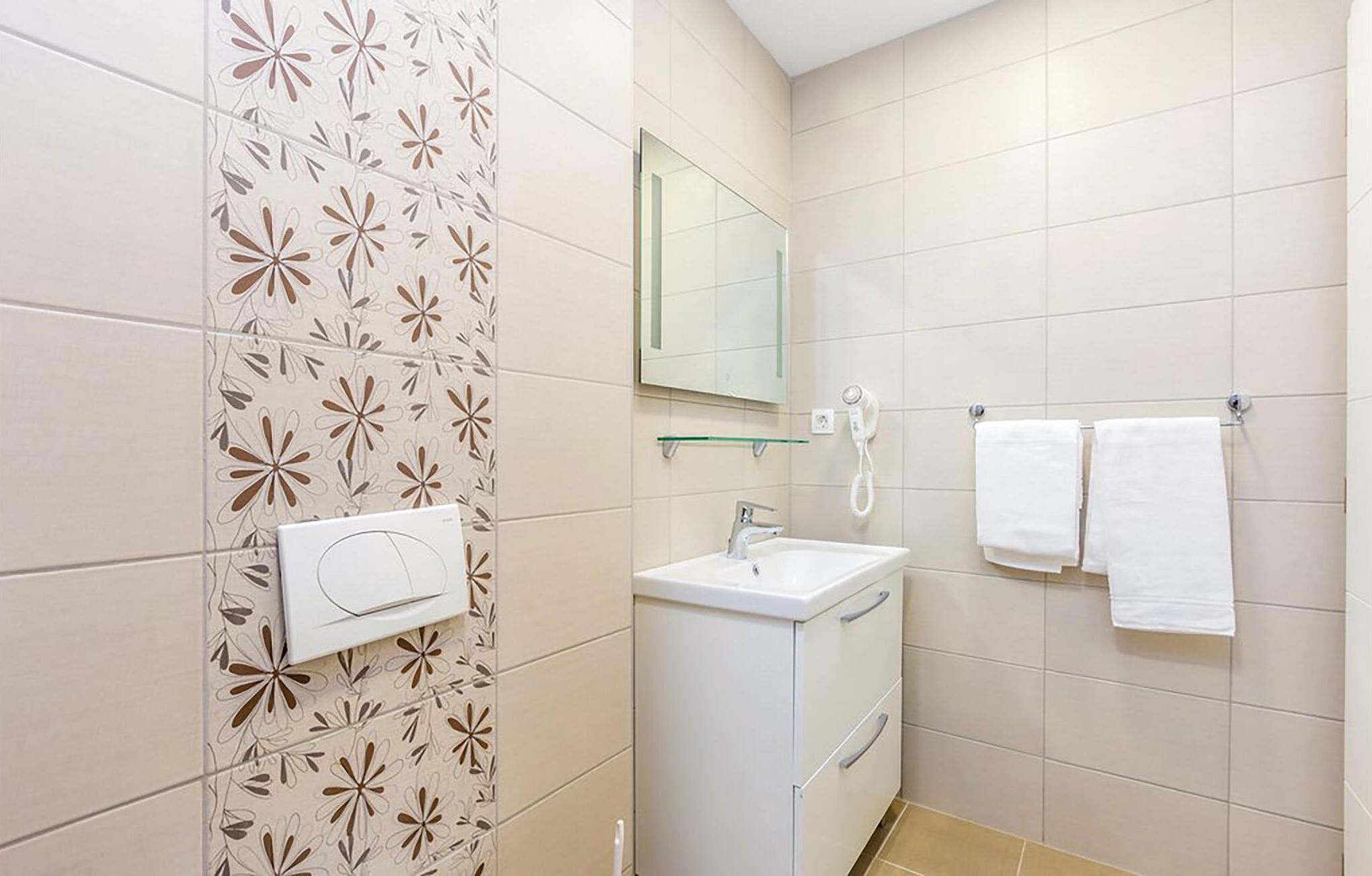A bathroom with a white sink, a mirror, a hairdryer, and two white towels on a rack.
